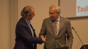 Ton Gorgels geeft Peter van Dijk een hand naast de presentatiemicrofoon